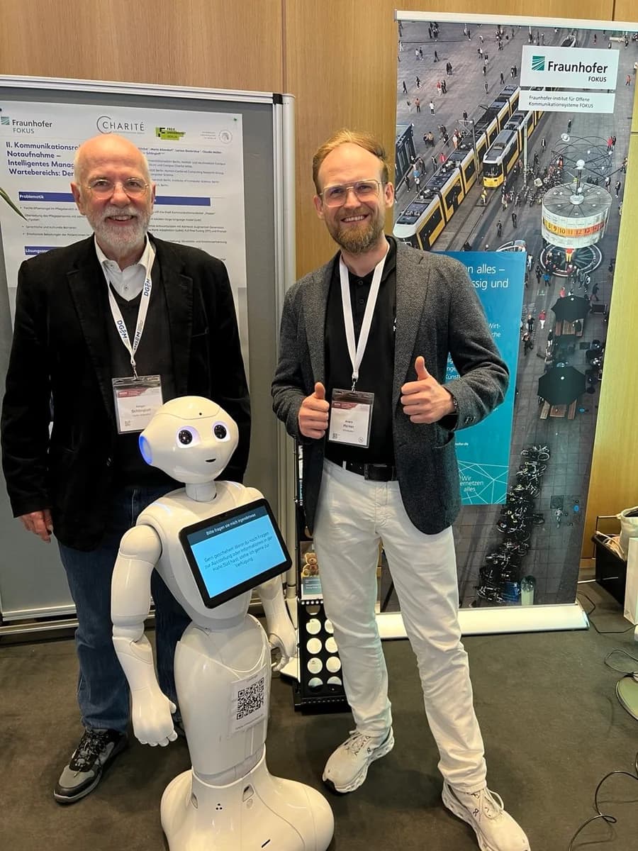 André Heiner mit dem humanoiden Pepper-Roboter vor Fraunhofer-FOKUS- und Charité-Bannern auf einer KI-Fachmesse zu Robotik im Gesundheitswesen