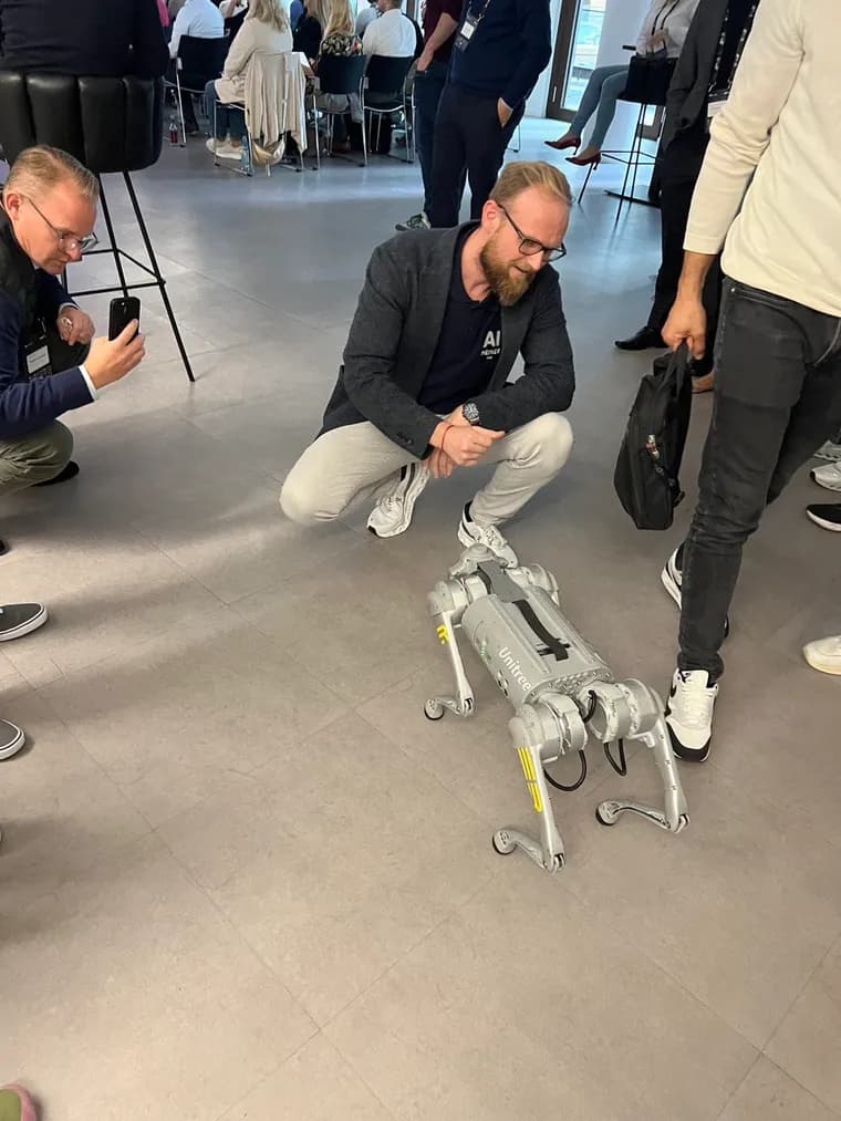André Heiner hands-on mit einem Unitree-Roboterhund bei einem KI-Event, Teilnehmer im Hintergrund
